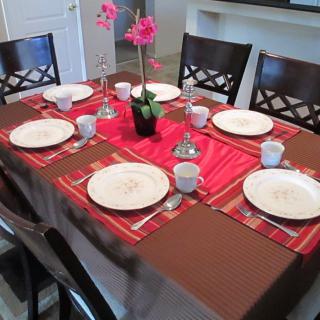A neatly set dining table with red and brown decor, featuring plates, glasses, and a floral centerpiece.