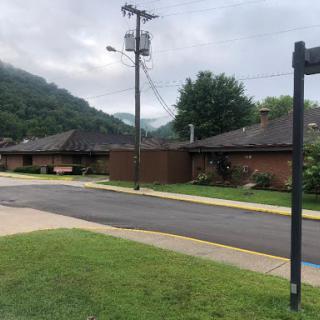 A peaceful neighborhood scene with buildings along a road, set against a backdrop of rolling hills.