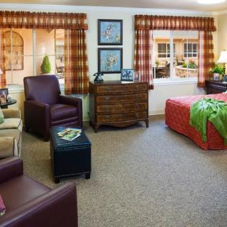 A cozy bedroom with comfortable seating, a bed with colorful bedding, and large windows allowing natural light.