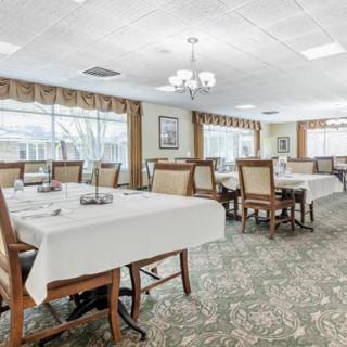 A spacious dining room with neatly arranged tables and chairs, featuring large windows and elegant table settings.
