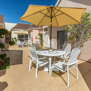 A serene outdoor patio setting with a table, chairs, and a large umbrella providing shade.