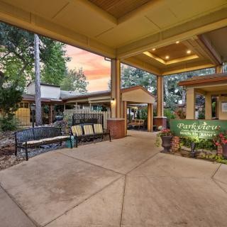 A welcoming entrance area featuring benches and plants under a covered walkway, set against an evening backdrop.