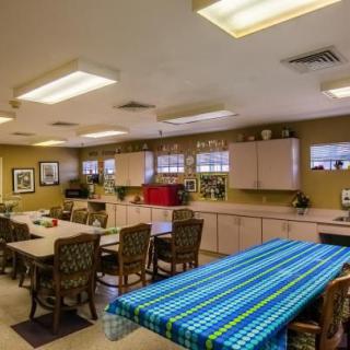 A well-lit communal kitchen and dining area with tables, chairs, and kitchen cabinets.