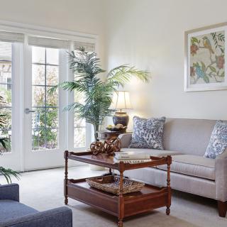 A cozy living room with neutral tones, featuring a sofa, a wooden coffee table, and elegant decor, bathed in natural light from large French doors.