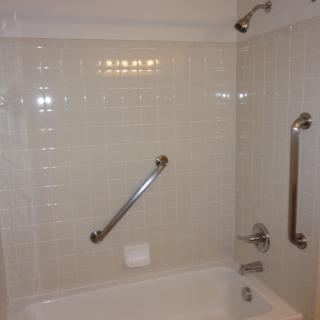 A bathroom with a bathtub featuring grab bars and tiled walls.