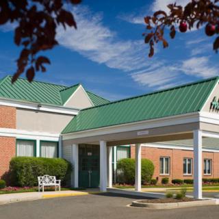A building entrance with a green roof and brick exterior, featuring a white canopy and a bench next to the entrance.