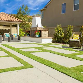 A well-maintained backyard with a patio, outdoor seating, and a paved walkway surrounded by lush greenery.