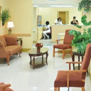 A comfortable waiting room with chairs, tables, and plants, adjacent to a reception desk.