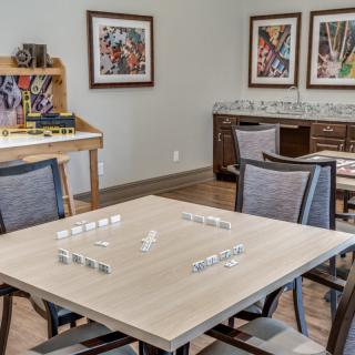 A cozy game room with a table set for dominoes, surrounded by chairs and decorated with colorful artwork.