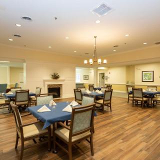 A cozy dining room with neatly arranged tables and chairs, featuring warm lighting and a wooden floor.