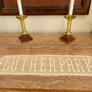 A decorative lace doily placed on a wooden table with two brass candlesticks.