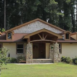 A charming single-story house surrounded by trees, featuring stone accents and a well-kept lawn.