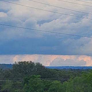 A dramatic view of the sky showcasing various cloud formations against a backdrop of greenery.