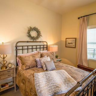 A cozy, well-decorated bedroom featuring a comfortable bed with pillows and throws, two lamps on side tables, and a window with curtains.