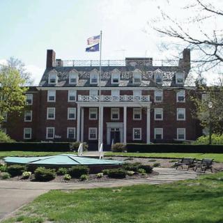 A brick building with a flag on top, surrounded by a well-maintained lawn and trees.