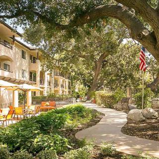 A well-landscaped apartment complex with outdoor seating and a pathway under large trees.