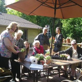 A group of people enjoying a sunny day on the patio, surrounded by plants and gardening supplies.