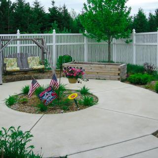 A well-maintained patio garden with various flowers and a white fence.