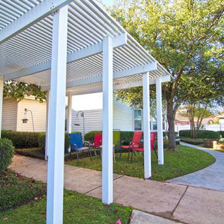 A backyard patio area with a white pergola and colorful chairs.
