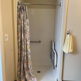 A bathroom with a shower stall, floral curtain, handrails, and a towel hanging on the wall.