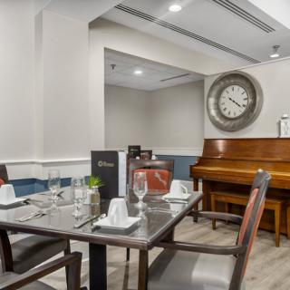 An elegant dining area with a neatly set table, a piano, and a large decorative clock on the wall.