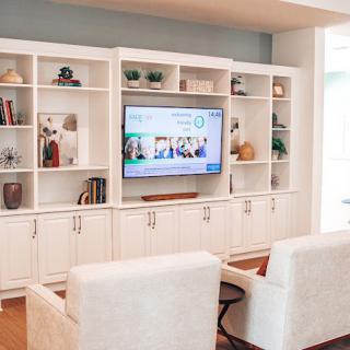 A cozy living room featuring a built-in entertainment center with open shelves, displaying various decorative items and a large television.
