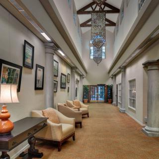 A spacious and elegantly designed hallway featuring plush chairs, artwork on the walls, and decorative lighting fixtures.