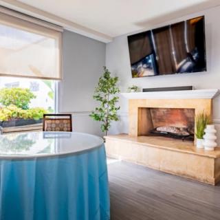 A modern living room featuring a fireplace, wall-mounted television, and a table draped with blue cloth.