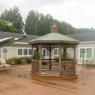 A wooden gazebo on an outdoor deck surrounded by patio furniture.
