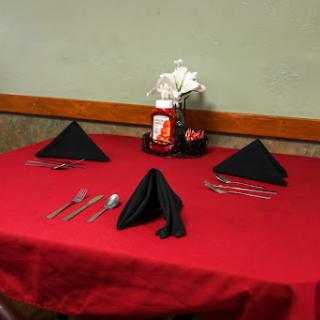 A neatly arranged table setting with a red tablecloth, black napkins, utensils, and a ketchup bottle.