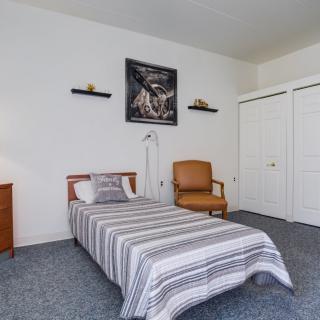 A minimalist bedroom with a single bed, chair, and decorative artwork on the wall.