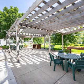 A serene outdoor patio featuring a wooden pergola, inviting furniture, and dappled sunlight.