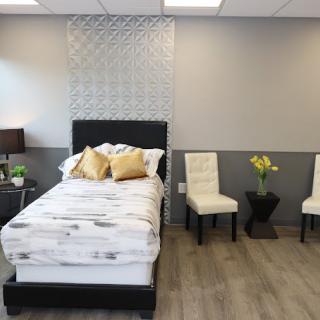 A modern bedroom with a bed, decorative pillows, and chairs, featuring contemporary decor.