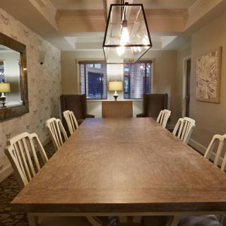 A well-decorated dining room featuring a large wooden table surrounded by white chairs, with elegant lighting and wall decor.