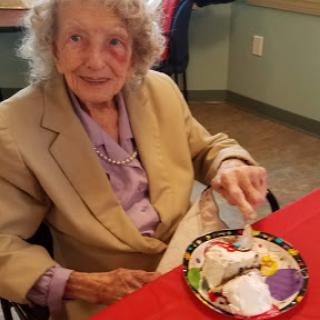 An elderly woman enjoying a dessert at a communal dining setting.
