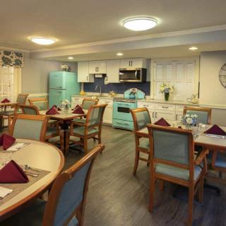 A cozy dining area with multiple tables and chairs, featuring a kitchen setup with vintage-style appliances.