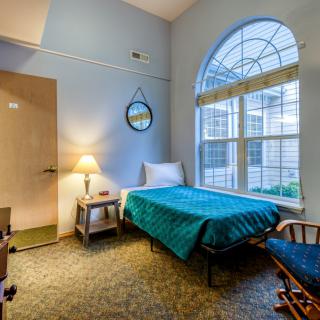 A cozy bedroom with a single bed, large arched window, and a small nightstand lamp.