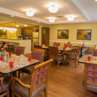 An inviting dining room with neatly arranged tables and chairs, warm lighting, and decorative artwork on the walls.