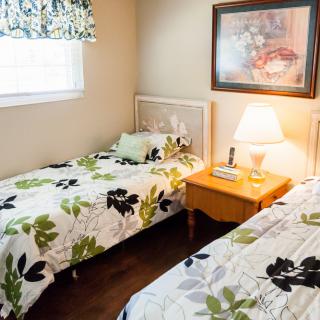 A cozy bedroom with twin beds and floral bedding, featuring a nightstand with a lamp and wall art above.