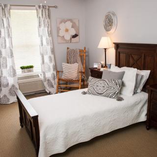 A cozy bedroom with a single bed, wooden furniture, and soft lighting.