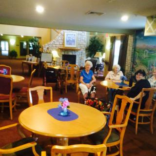 A cozy common area with seniors seated around tables in a senior living facility.