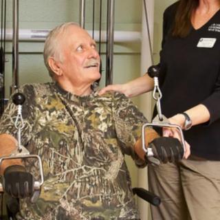 An elderly man engages in physical therapy with the help of a healthcare professional.