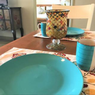 A dining table set with turquoise plates, a mosaic vase, and blue cups.