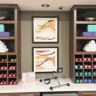 A well-organized exercise room with colorful dumbbells, neatly folded towels, yoga blocks, and abstract artwork on the wall.