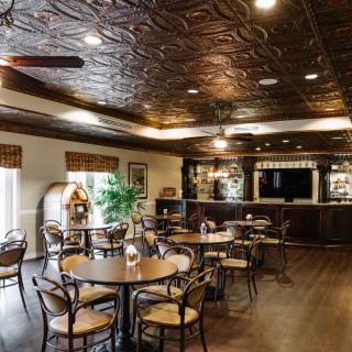 A cozy restaurant interior featuring a decorative ceiling, wooden tables and chairs, and a bar area.