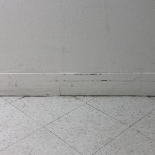 A section of a tiled floor with visible scuff marks along the baseboard.