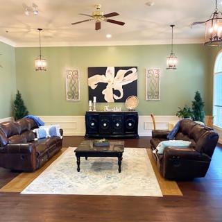 A well-decorated living room featuring leather sofas, a central coffee table, and wall art, all framed within a warm color palette and elegant lighting.