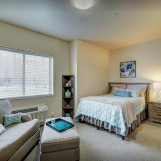 A cozy and well-lit bedroom featuring a comfortable bed, a small sitting area, and decorative elements.
