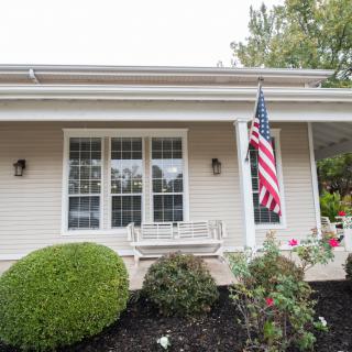 A house with a front porch, displaying an American flag and surrounded by greenery.