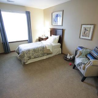 A cozy bedroom with a single bed, armchair, and decorative artwork.